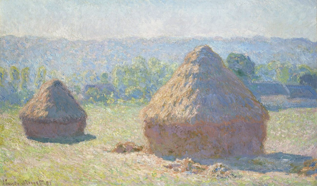 Two haystacks stand in an open field, surrounded by late-summer colour and distant hills.